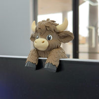 Brown Highland cow monitor buddy sitting on top of a computer screen