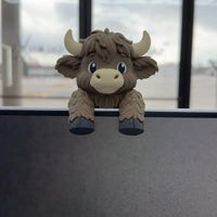 Highland cow screen sitter perched on a monitor edge